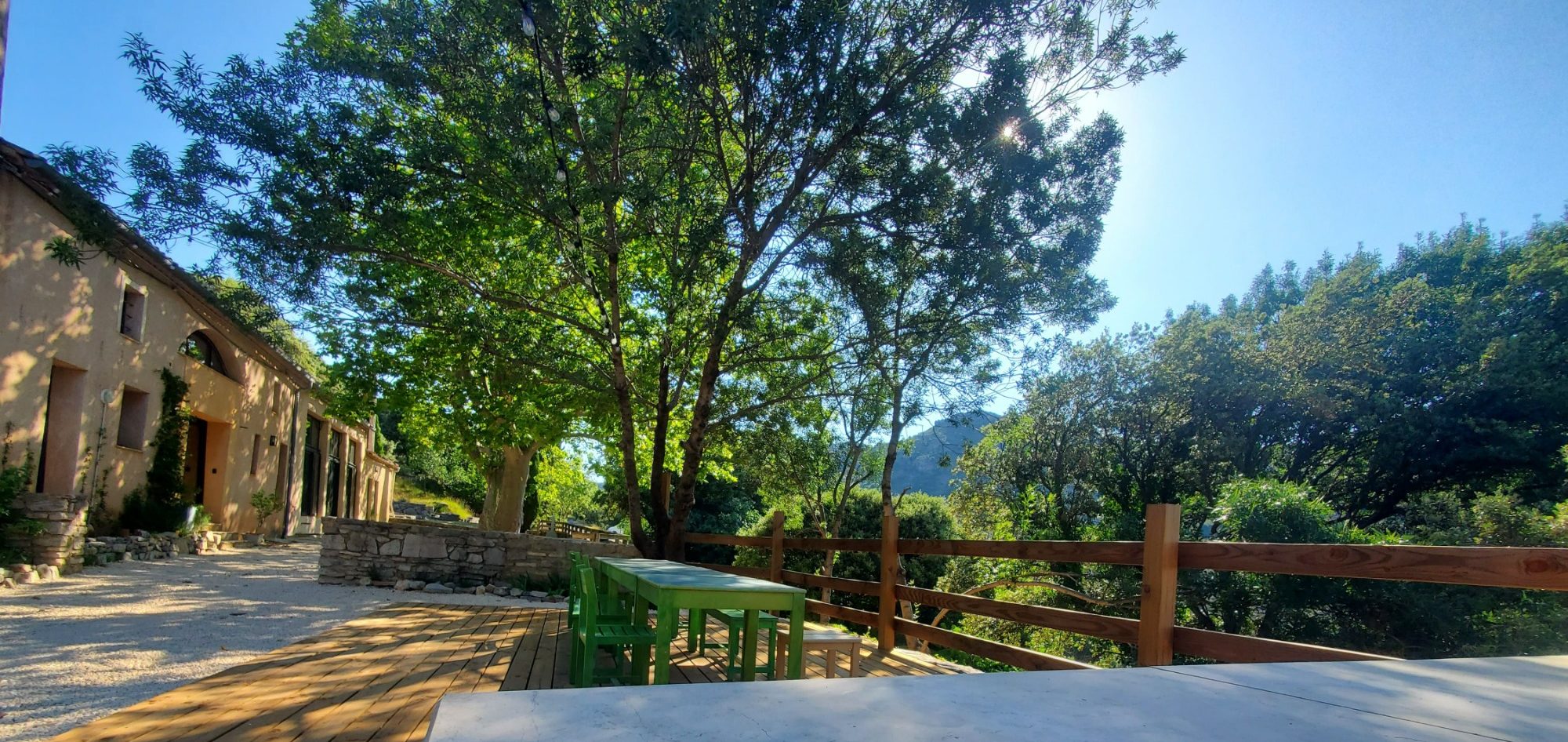 terrasse en bois 48m2 Vue d'une terrasse ombragée et une maison en arrière-plan sous un ciel bleu.